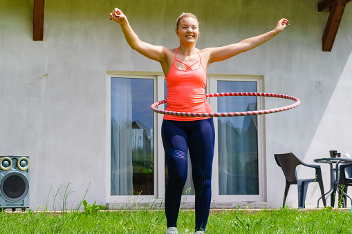 Woman using hoola hoop for slim waist, doing exercises gym outdoor in garden. Workout sport and training.