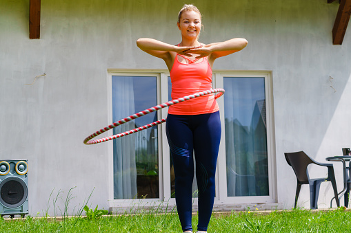 Woman using hoola hoop for slim waist, doing exercises gym outdoor in garden. Workout sport and training.