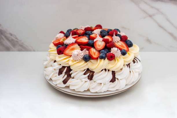 ciasto pavlova z bitą śmietaną, sosem czekoladowym, świeżą truskawką, jagodami i malinami, udekorowane bezami na jednolitym tle - large cheese beautiful red zdjęcia i obrazy z banku zdjęć