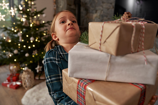 Elementary age girl barely carrying a pile of Christmas presents