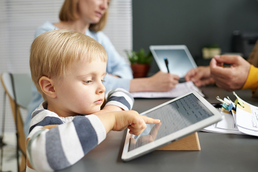 Little boy playing on tablet pc while his mother talking to social worker in office