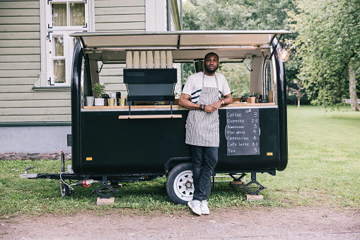 A confident and positive small business owner, standing with his coffee trailer for a portrait.
