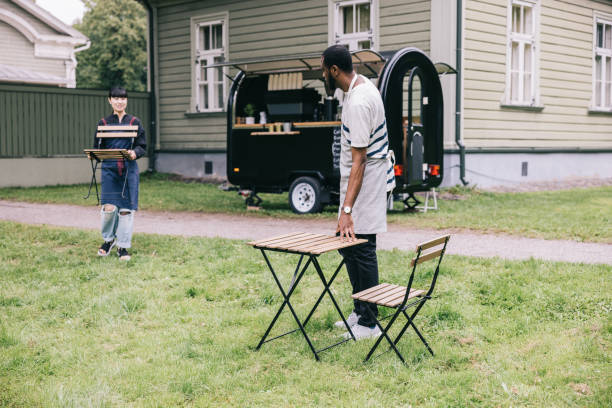African entrepreneur and his Japanese partner showcase unity and entrepreneurship as they open their charming mobile coffee trailer, bringing out table and chairs
