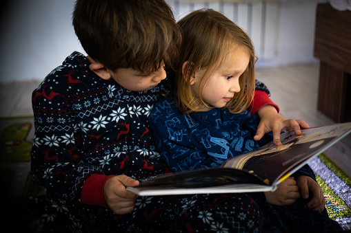Brother and sister read book in pyjamas bare feet evening sleep family