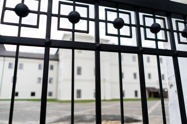 istock Big white Building and low sun shining seen through the gate. View through fence 1818443603