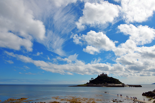 Marazion, Cornwall, England, UK: St Michael's Mount and dreamtic sky - tidal island on the southwestern tip of England, lying south the town of Marazion in Cornwall. It can be reached either by ferry or, at low tide, via a narrow causeway from Marazion. St Michael's Mount combines many features of Cornwall's geology, It consists of the top area of a granite intrusion, which penetrated into weakly metamorphic shales (metapelites) of the Devonian. The southern part of the granite is crossed by steep veins with greisen mineralization. The older formations are rich in the minerals tourmaline, wolframite and cassiterite. The sea-facing outcrops have been designated as a Site of Special Scientific Interest since 1995 and are under protection - Cornwall Area of Outstanding Natural Beauty