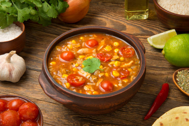 Easy Mexican chicken and rice soup in a terracotta soup bowl on a rustic wooden table with ingredients. stock photo