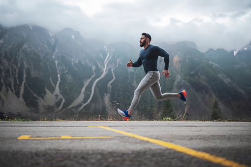 Side view of sportsman running on the road with foggy hill in background, he running outdoor in autumn season, Outdoor workout, Full Length