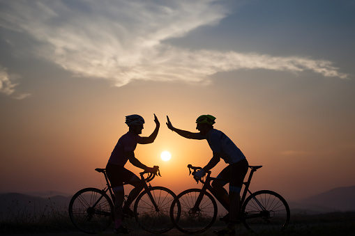 Happy athlete men on racing bicycle on sunset.