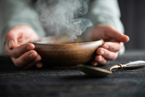 Woman hand holding fresh soup in wooden bowl