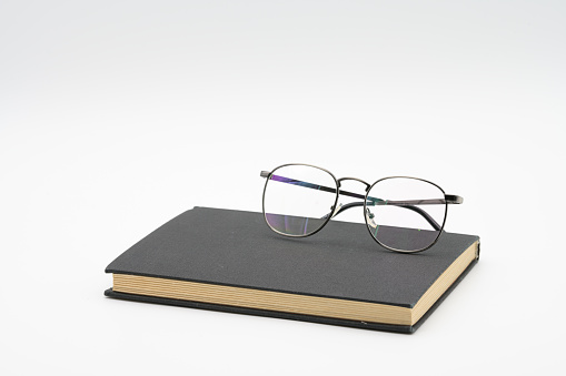 Reading glasses with colored glass staying on black book isolated on white background