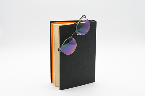 Reading glasses on Standing black book with orange inlay isolated on a white background