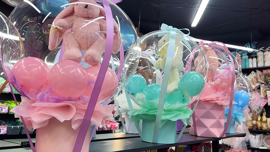 Transparent gift box with colorful balloons and soft toy bunnies inside for birthday and other holiday events in gift and decoration shop. Gift big box with a toy in a boutique.