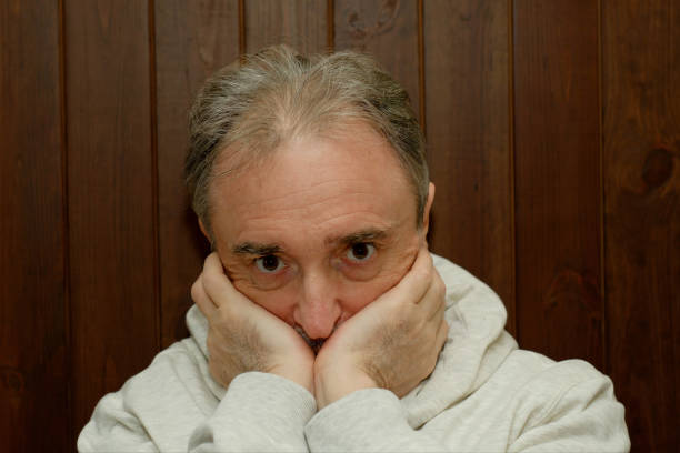 Portrait of an elderly unshaven man with a mustache in a light hoodie on a brown wooden background