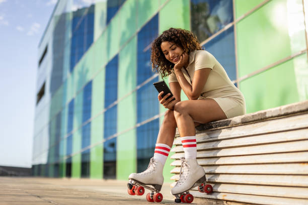 istock Young beautiful Spanish woman on roller skates during a summer day, resting next to a modern building in the city center 1818489430
