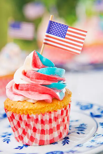 Red-white-and-blue cupcakes with American flags on an outdoor table.