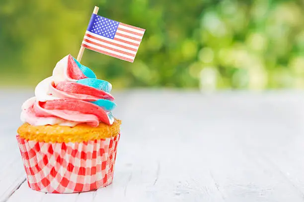 Red-white-and-blue cupcake with an American flag on an outdoor table.