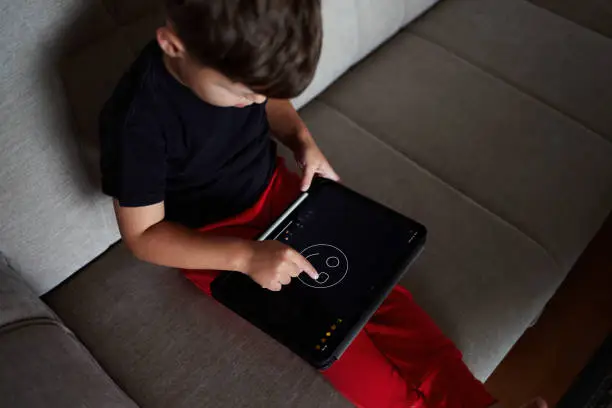 Photo of Toddler draws on a tablet using a finger at home.