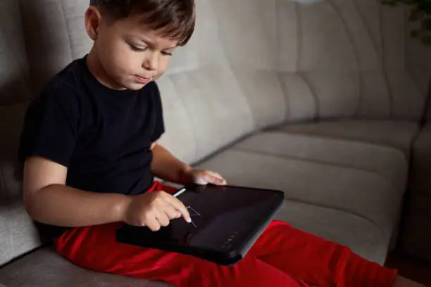 Photo of Toddler draws on a tablet using a finger at home.