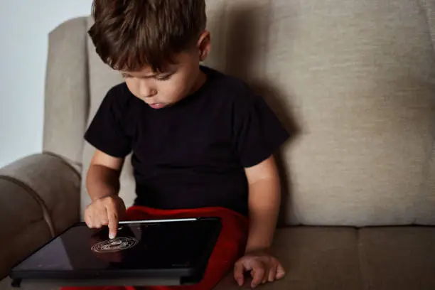 Photo of Toddler draws on a tablet using a finger at home.