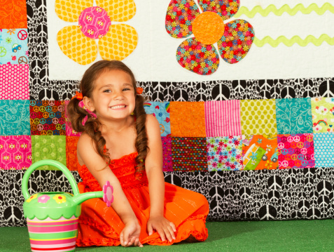 Cute little girl sitting with a watering can. Colorful flower background.