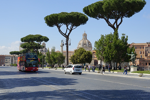Passing red tourist bus and tourists walking along Fori Imperiali Street in Rome, Italy