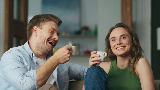 Laughing lovers coffee cups holding at home closeup. Carefree spouses having fun