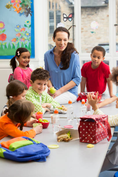 Young Students at Lunchtime Mixed group of ethnic kids having lunch with teacher food elementary student healthy eating schoolboy stock pictures, royalty-free photos & images