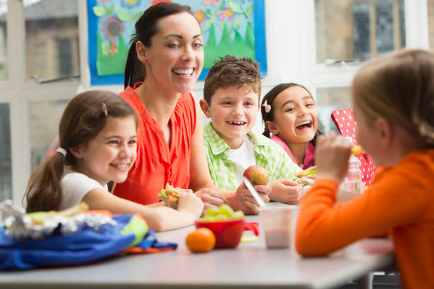 Young Students at Lunchtime Mixed group of ethnic kids having lunch with teacher cafeteria sandwich food healthy eating stock pictures, royalty-free photos & images