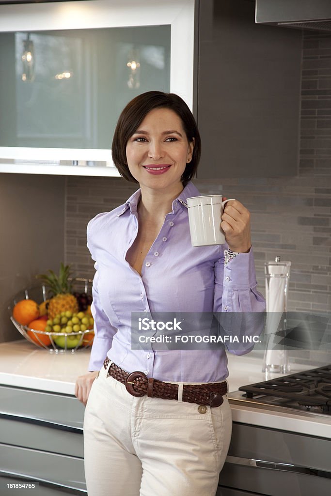 Young woman in the kitchen "Young Caucasian woman in her new new luxury kitchen.Objects on the wall shelf are not copyright pieces of art, but ordinary furniture store prop." Adult Stock Photo