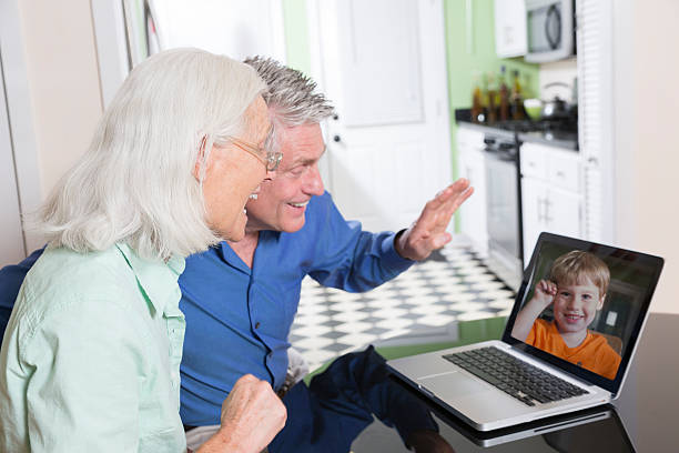 A senior couple use a laptop computer at home to video-chat with their grandson.