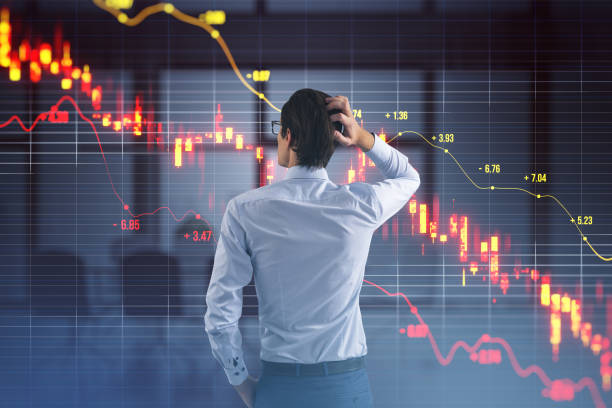 istock Back view of stressed young businessman with downward red candlestick forex chart with index on blurry office interior background. Crisis, falling stock market and recession concept. Double exposure. 1818551359