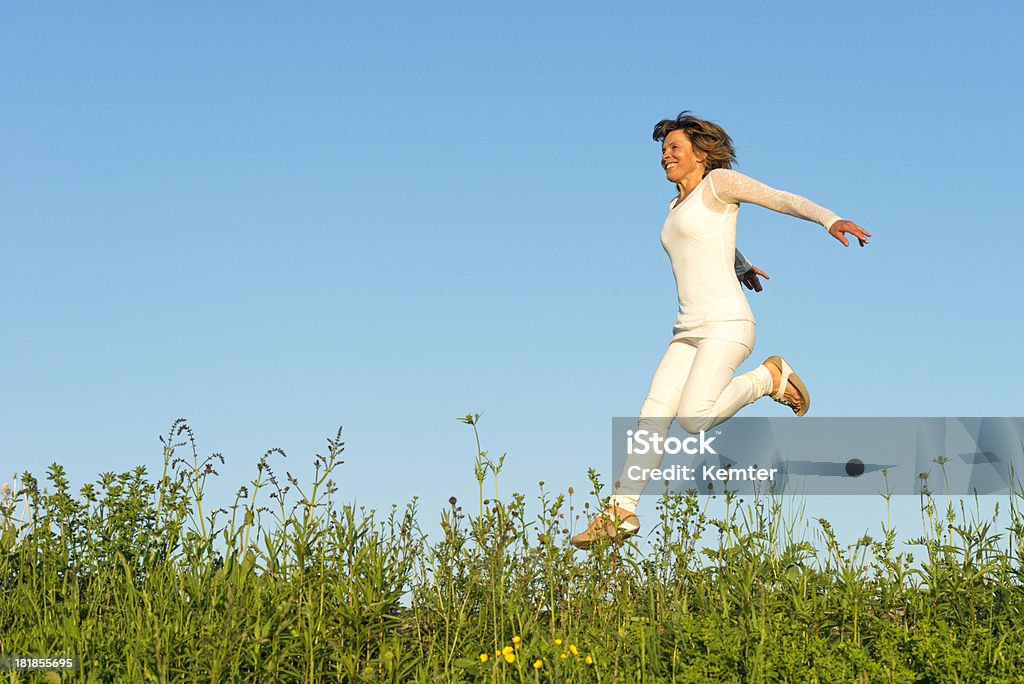 happy woman running on meadow smiling mature woman in white jumping on meadow Jumping Stock Photo