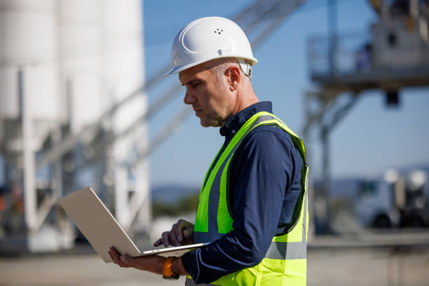 istock Portrait of serious male engineer with hardhat using laptop while working at industrial facility 1818561864