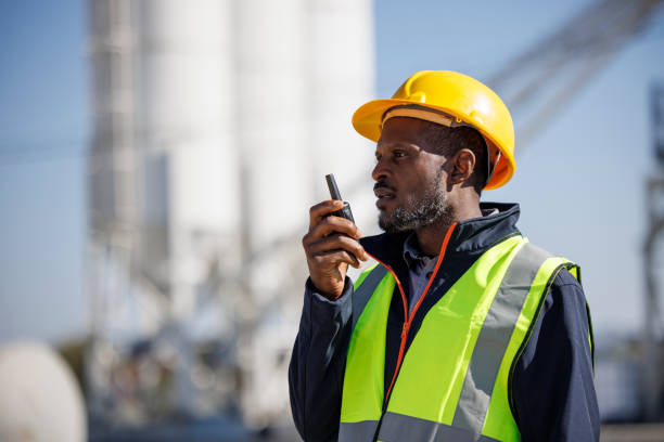 porträt eines industriearbeiters oder ingenieurs, der walkie-talkie in einer industrieanlage verwendet - construction safety mid adult men road construction stock-fotos und bilder