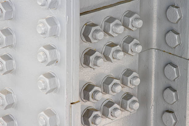 Seen here is a corner intersection of large steel support beams. The beam and hardware are painted grey and contains multiple nuts and bolts.