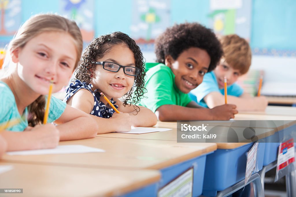 Elementary school children writing in class Multi-ethnic elementary school children writing in classroom.  Focus on Hispanic girl wearing eyeglasses (8-9 years). Classroom Stock Photo