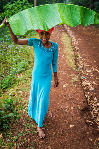 Little girl hiding from rain under banana leaf in a remote village, Central Ethiopia, East Africa