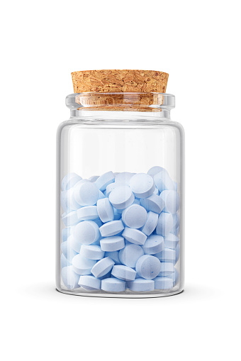 Blue pills in middle size transparent glass jar isolated on white background. Natural health supplement.
