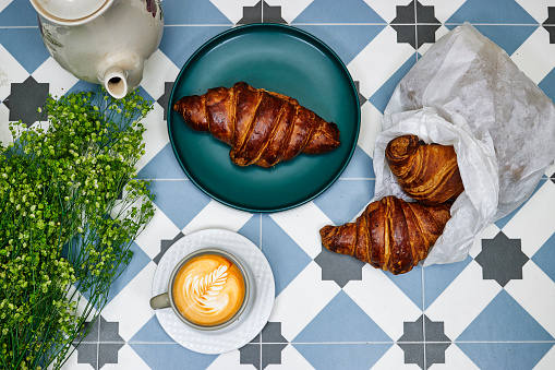 morning concept - Fresh baked croissant for breakfast, coffee cup with leaf late art on tiles table with green gypsophila