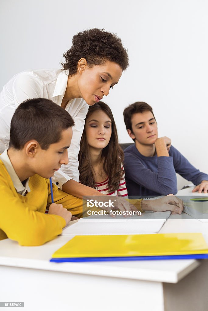 Teacher helping students Young mixed race teacher helping group of students with schoolwork. Adolescence Stock Photo