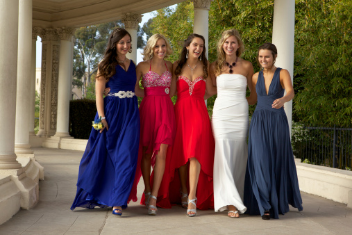 A group of five beautiful teenage girls ready for the prom are walking and smiling.