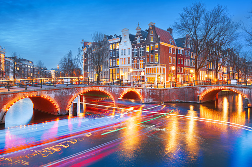 Amsterdam, Netherlands bridges and canals at twilight with light trails from passing boats.