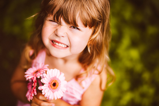 Lovely little girl pulling a face and holding pink flowers