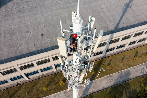 Engineer uses smartphone while repairing 5G signal tower