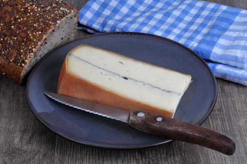 Piece of Morbier on a plate with a knife and seeded bread close-up