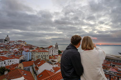 Alfama, Lisbon, Portugal - Nov 13, 2023: Young couple watch splendid sunrise at a high spot that overlooks the Tagus River and the harbor area.