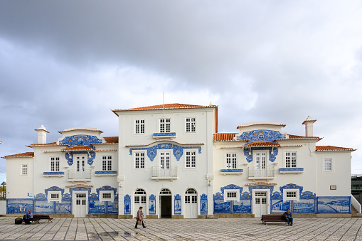 Aveiro, Portugal - Nov 7, 2023: A woman with umbrella walks in front of the lovely old azulejo tile decorated train station.