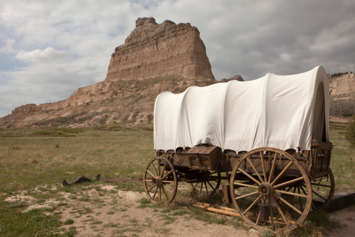 Storm clouds pass over an old covered Murphy Wagon on the Oregon Trail with Scotts Bluff in the background in Scotts Bluff National Monument in Nebraska.
