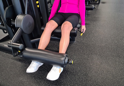 Girl does exercises in gym and does leg extension training on simulator. Sports fitness press and legs triceps